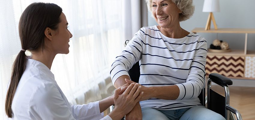 elderly woman in wheelchair smiling at nurse in skilled nursing facility.